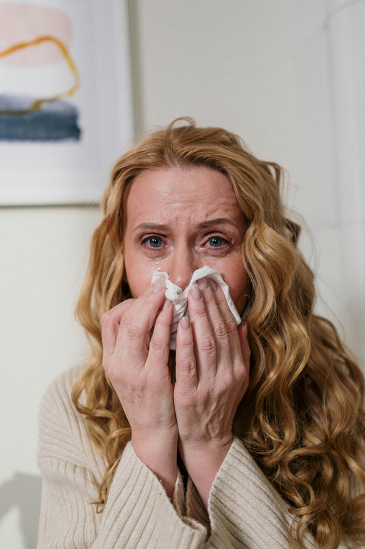 Woman with long curly hair sneezing into a tissue, showing signs of cat allergies indoors